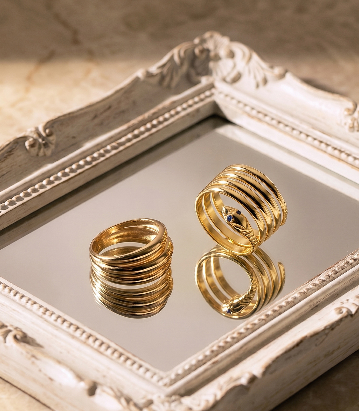 Deux bagues en or design serpent posées sur un plateau miroir